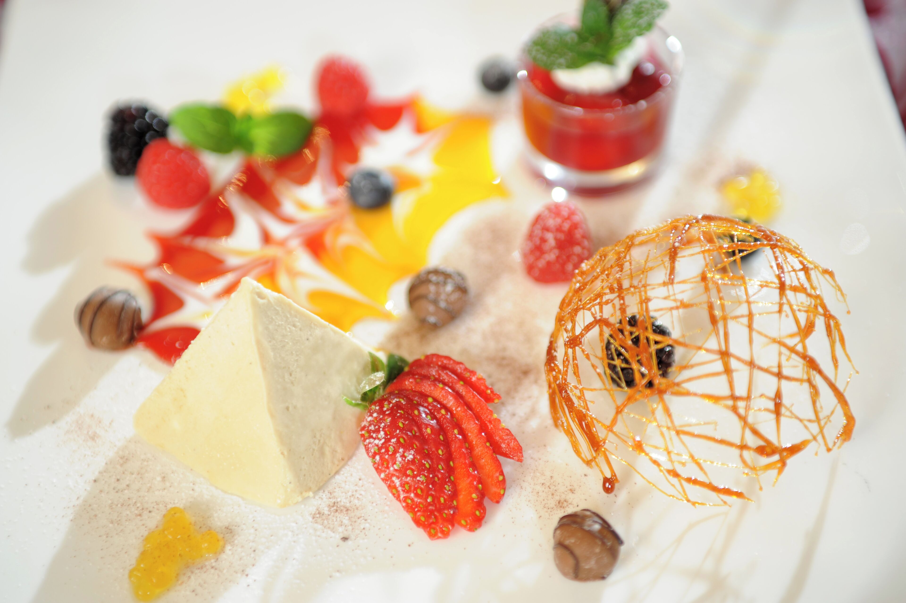 A dessert plate with various fruits and a small glass of red liquid.