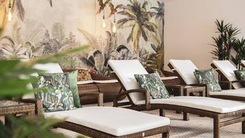 A room with wicker lounge chairs, a large tropical mural, and hanging light fixtures.