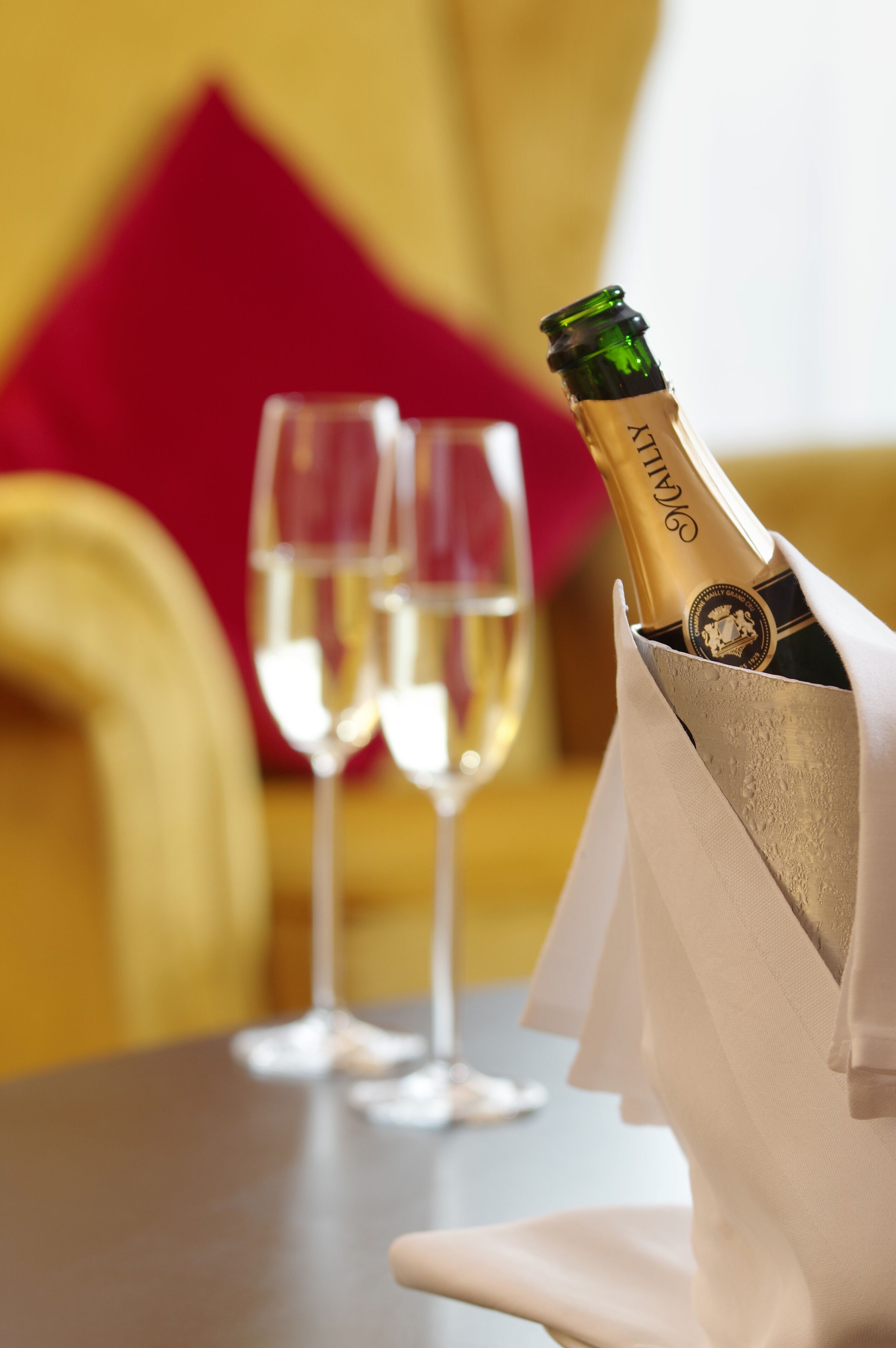 A bottle of champagne in a glass holder on a table with two empty champagne flutes.