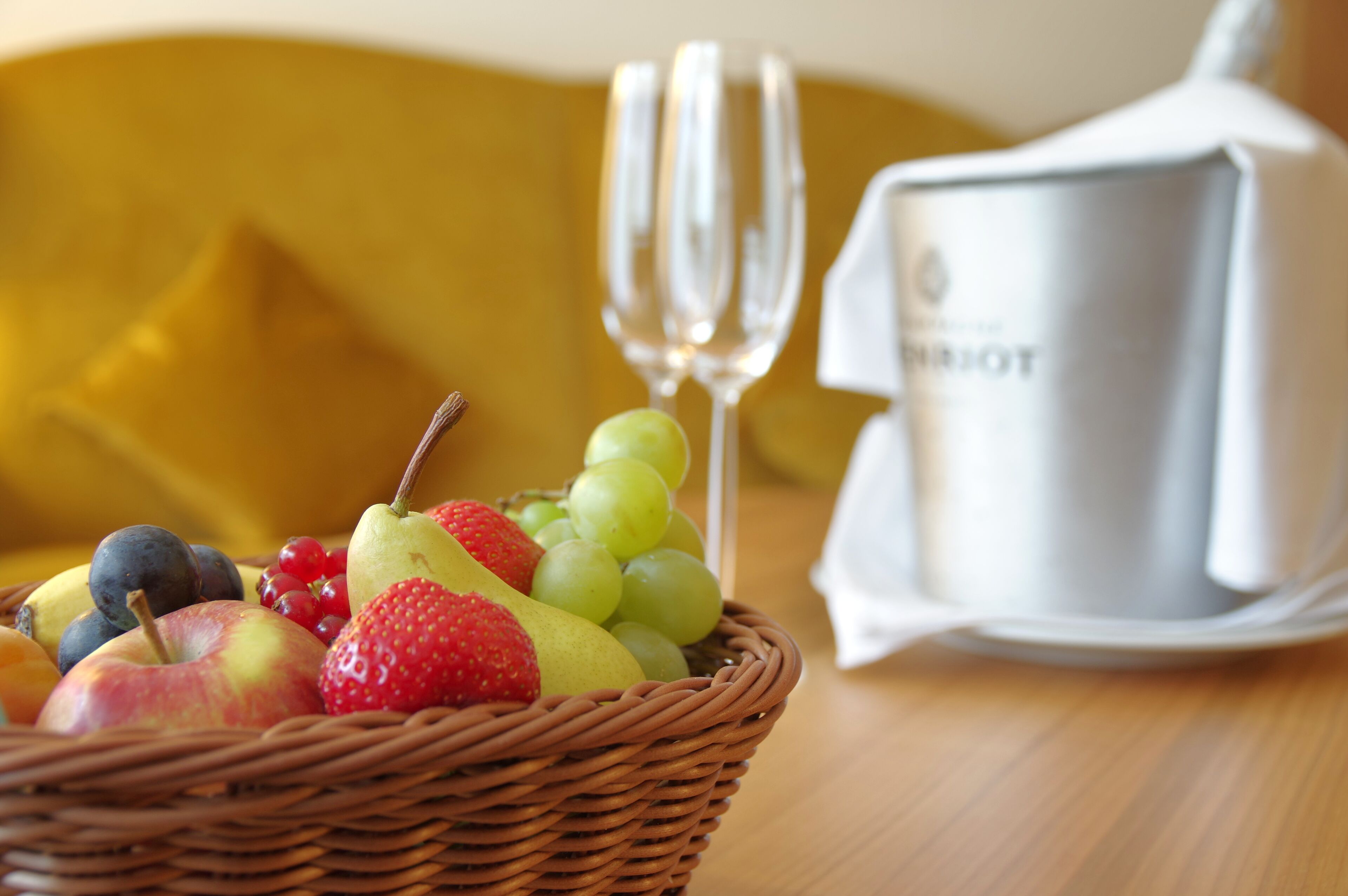 A wicker basket filled with fruits and two champagne flutes on a table.