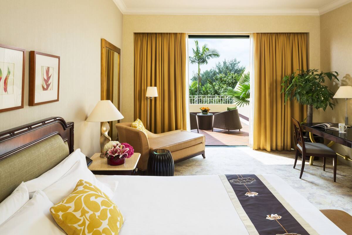 A hotel room with a bed, a sofa, a desk, and a balcony with curtains.
