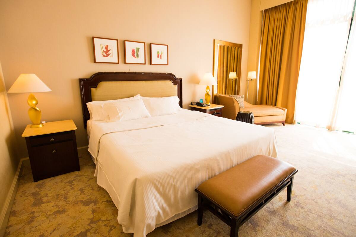 A hotel room with a large bed, bedside tables, a chair, and a bench.