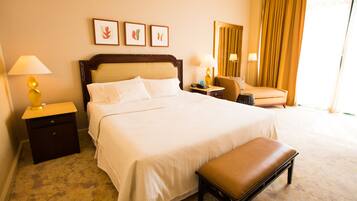 A hotel room with a large bed, bedside tables, a chair, and a bench.