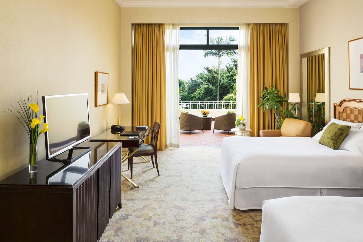 A hotel room with a bed, a TV, a desk, and a balcony with chairs.