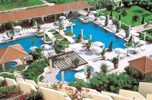 Un resort con una amplia piscina central, varias piscinas más pequeñas y zonas de estar al aire libre rodeadas de vegetación.