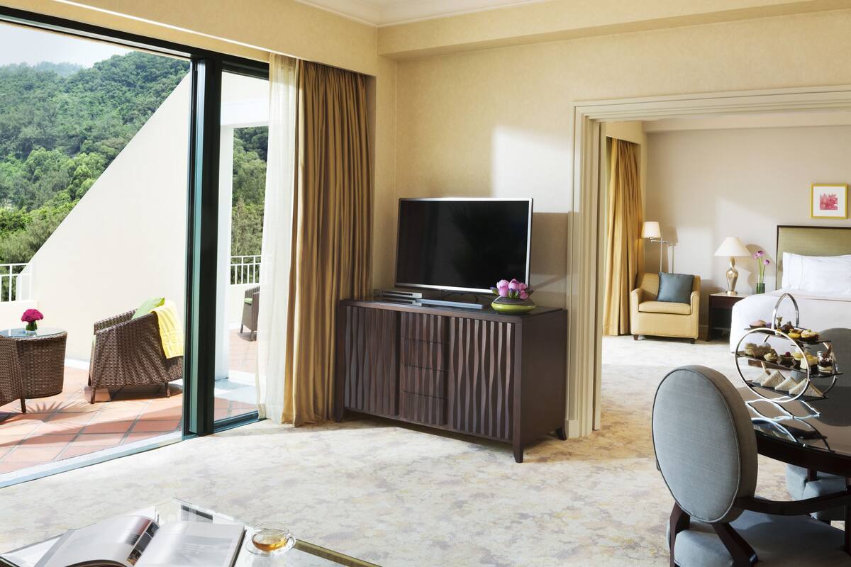 A hotel room with a large window, a flat-screen TV, a dining area, and a bed.