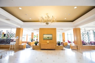 Un amplio vestíbulo con candelabro, un panel de madera central con una pintura y plantas en macetas.