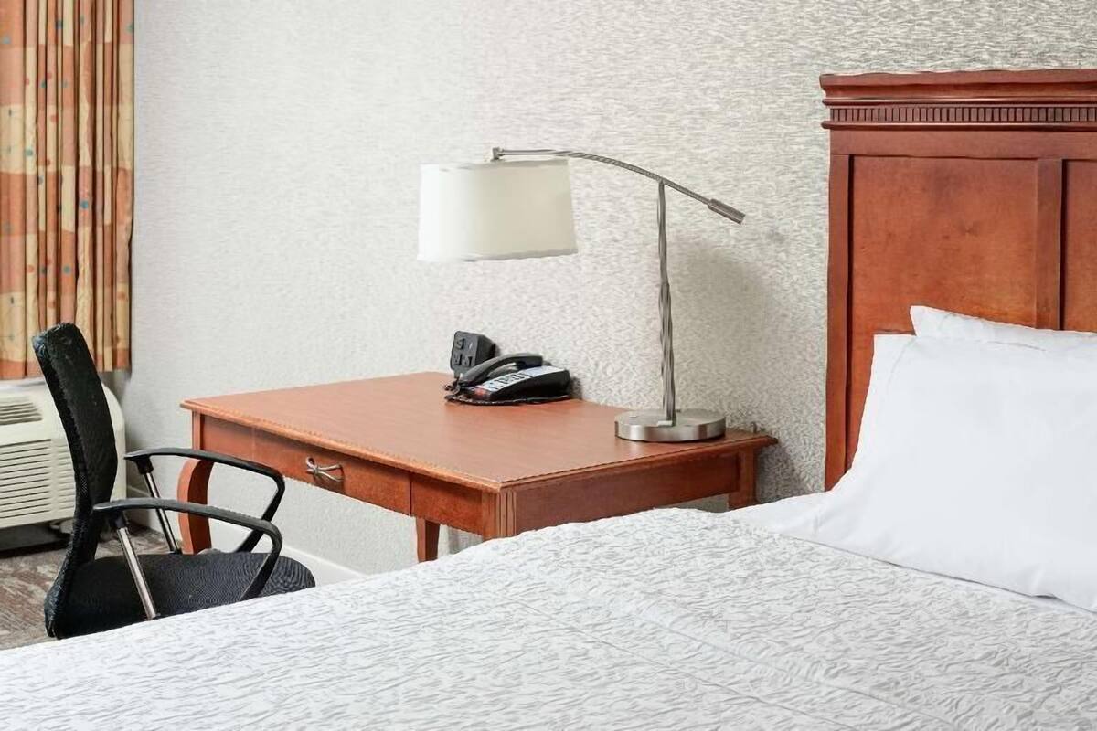 A hotel room with a bed, a desk with a lamp, a chair, and a telephone.