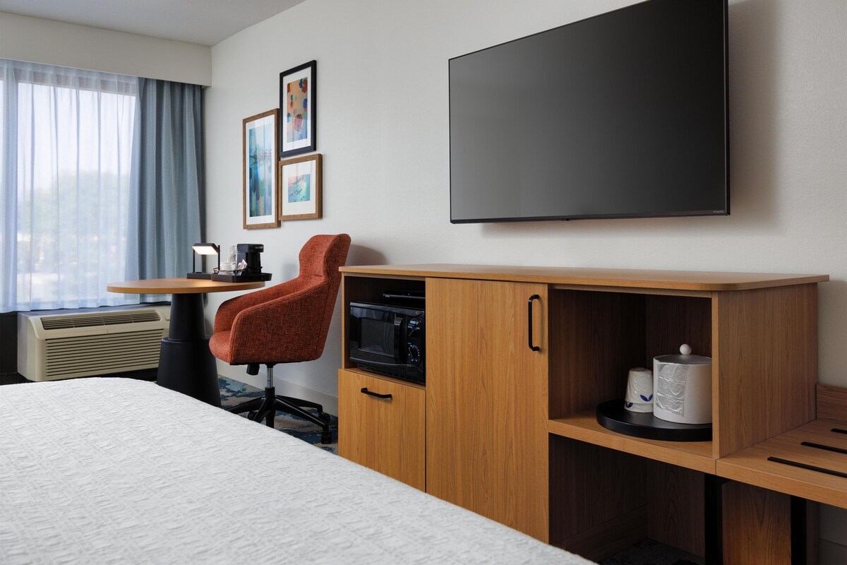 Habitación de hotel con cama, escritorio con silla, televisor de pantalla plana, microondas y cafetera.