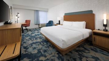 Quarto de hotel com uma cama grande, uma escrivaninha, uma cadeira, uma televisão e um abajur.
