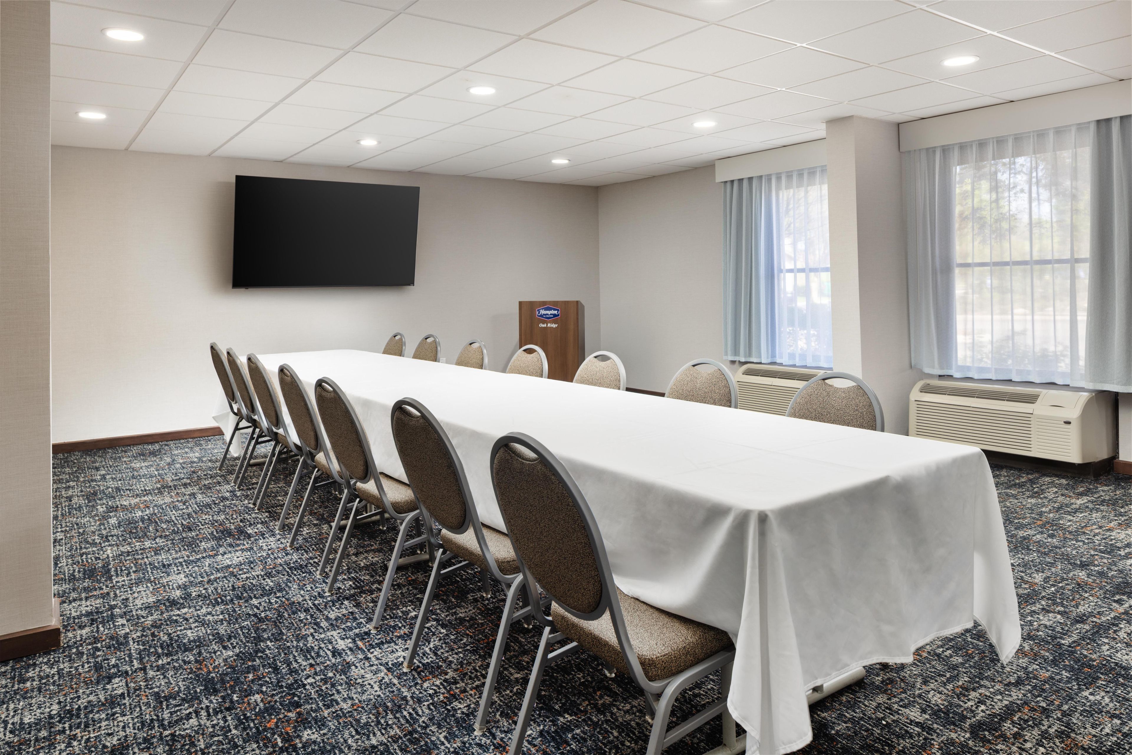 A conference room with a long table, chairs, a flat-screen TV, and air conditioning units.
