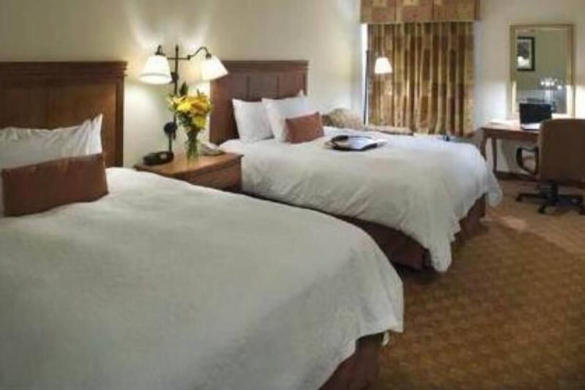 A hotel room with two beds, a desk, a chair, a lamp, and a window with curtains.