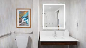 A bathroom with a white sink, a framed painting, a mirror with lights, and a handrail.