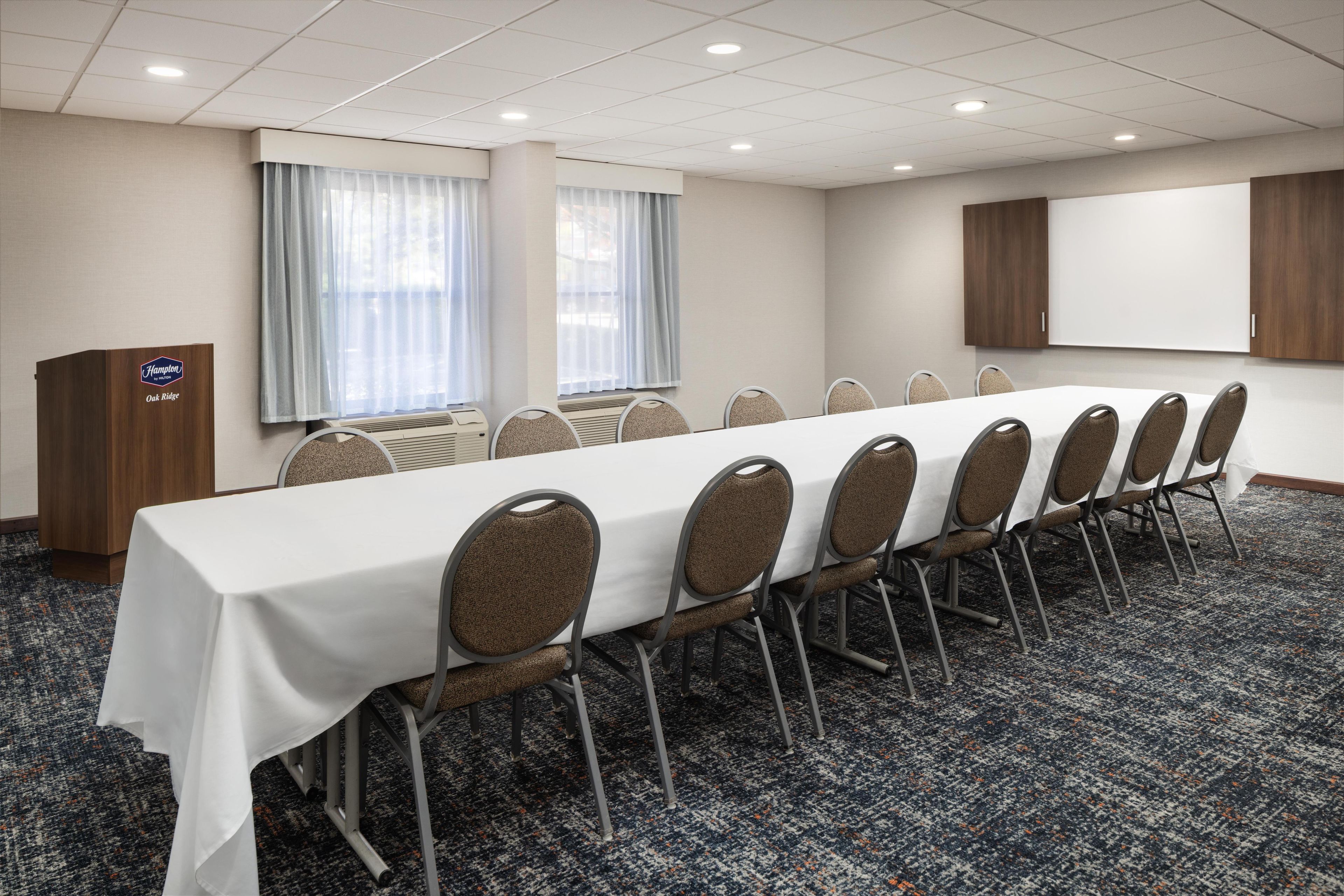 A conference room with a long table, chairs, a podium, and a large screen.