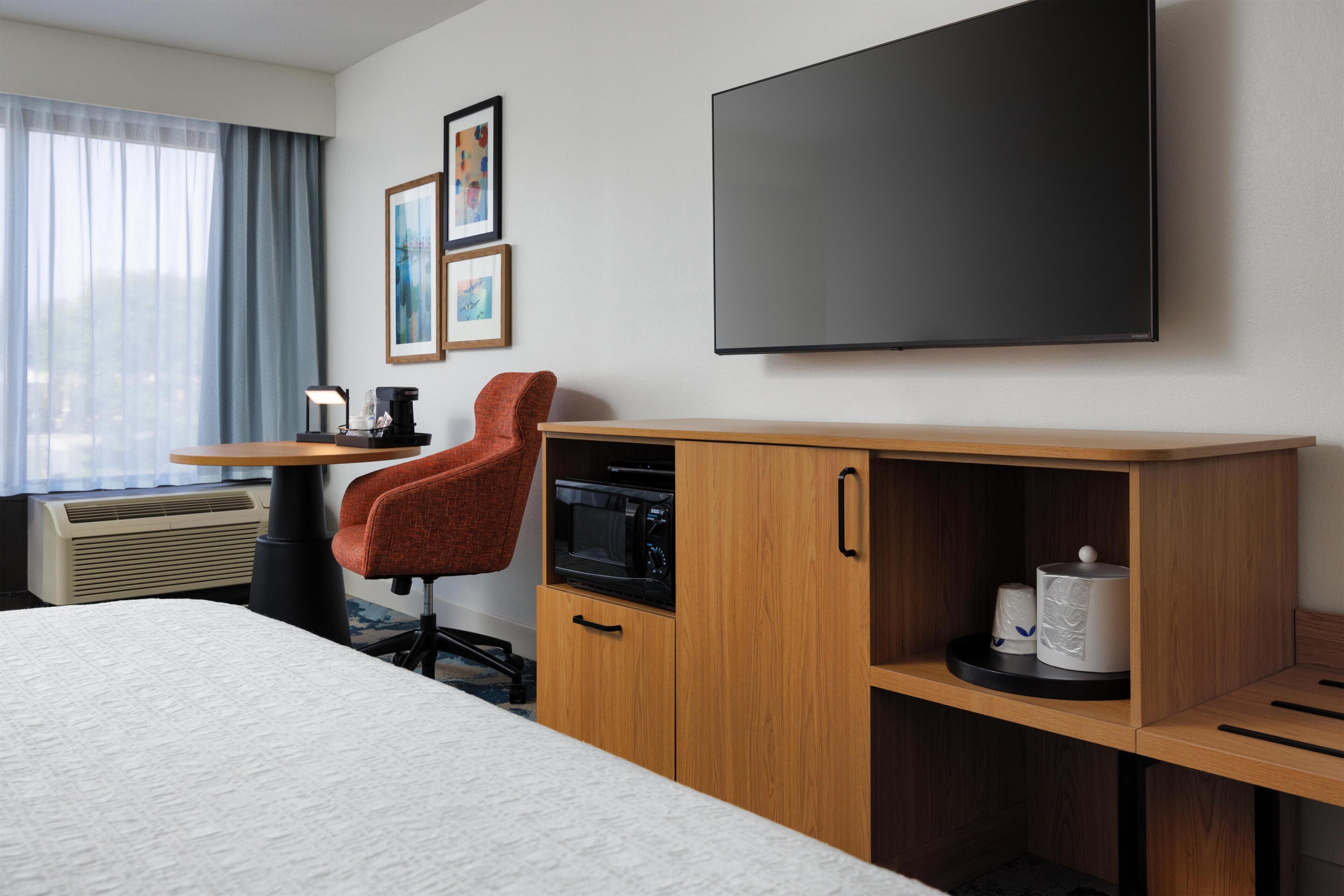 Une chambre d’hôtel équipée d’un lit, d’un bureau avec une chaise, d’un téléviseur à écran plat, d’un four à micro-ondes et d’une machine à café.