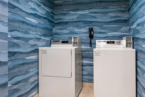 Two white wall-mounted washers with control panels, a phone, and a water heater in a room with blue wave-patterned wallpaper. - Hampton Inn Oak Ridge Knoxville (Oak Ridge)