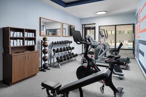 A gym with exercise equipment, a mirrored wall, and a wooden cabinet with towels. - Hampton Inn Oak Ridge Knoxville (Oak Ridge)