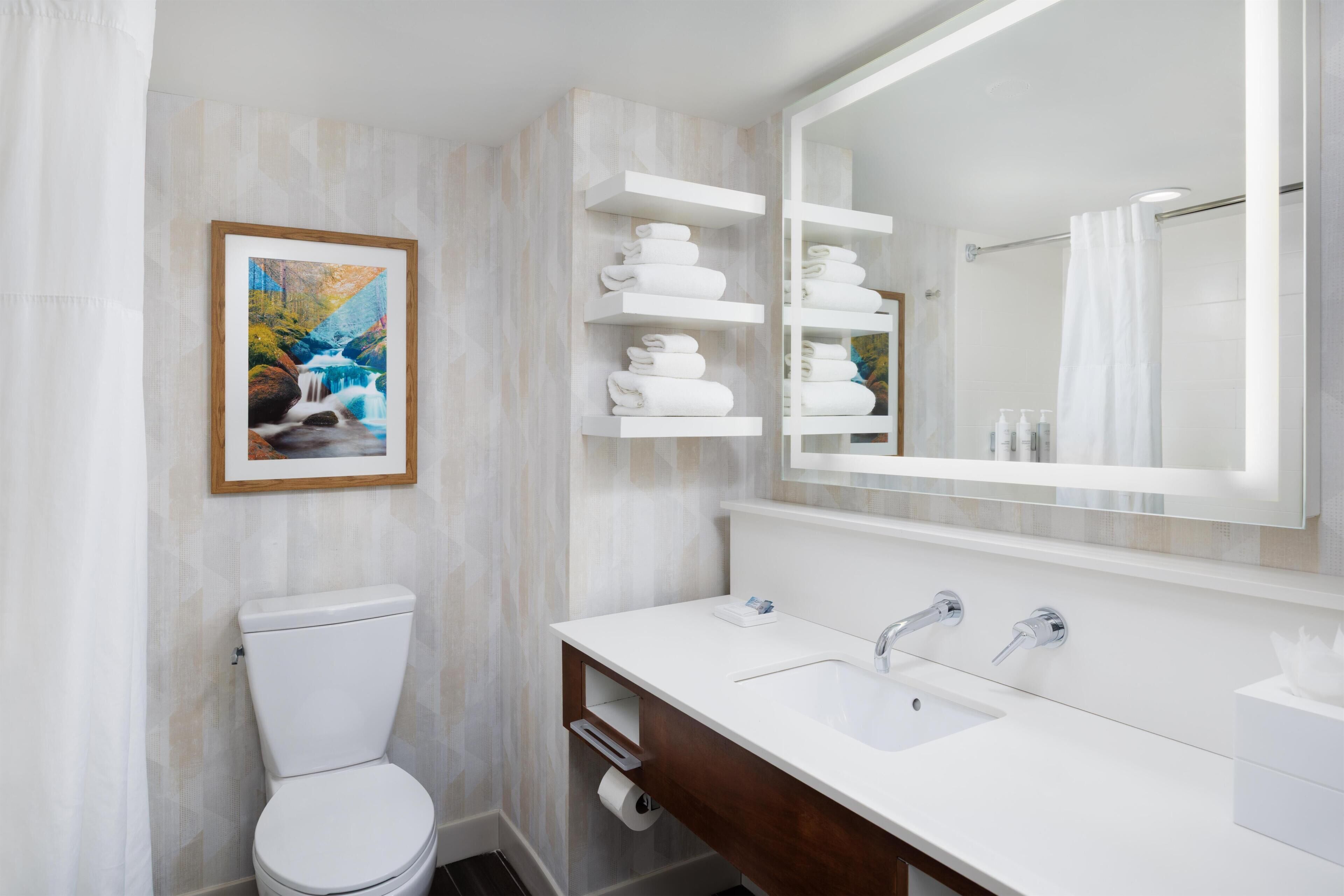 Un baño moderno con inodoro, lavamanos, espejo y toalleros.