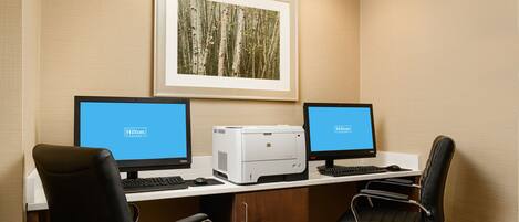 A hotel office with two computer desks, each with a monitor and keyboard, and a printer between them.