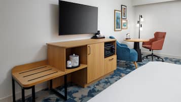 A hotel room with a bed, a desk with a chair, a TV, and a small table with a chair.