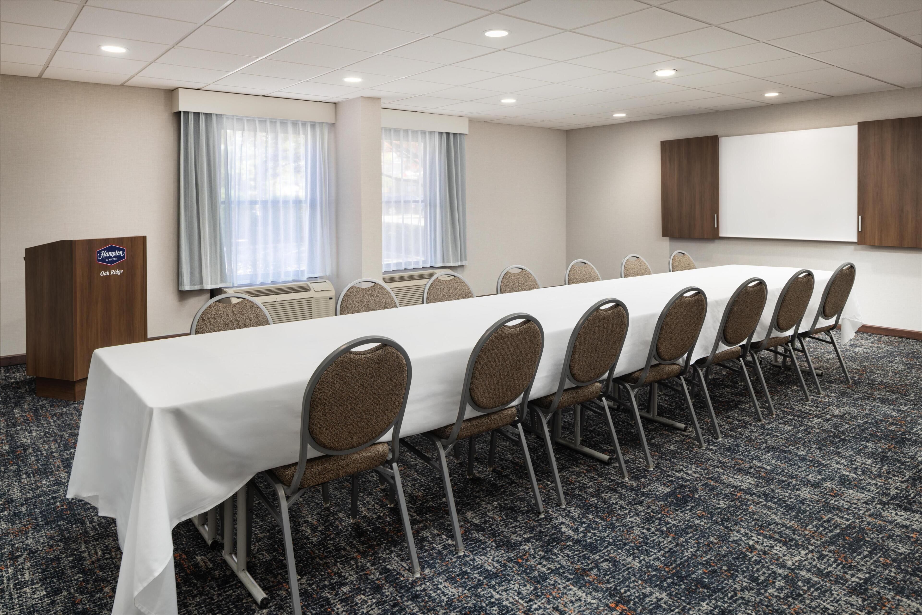 Un salón de conferencias con una larga mesa, sillas, un atril y una pantalla grande.