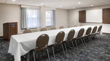 Un salón de conferencias con una larga mesa, sillas, un atril y una pantalla grande.