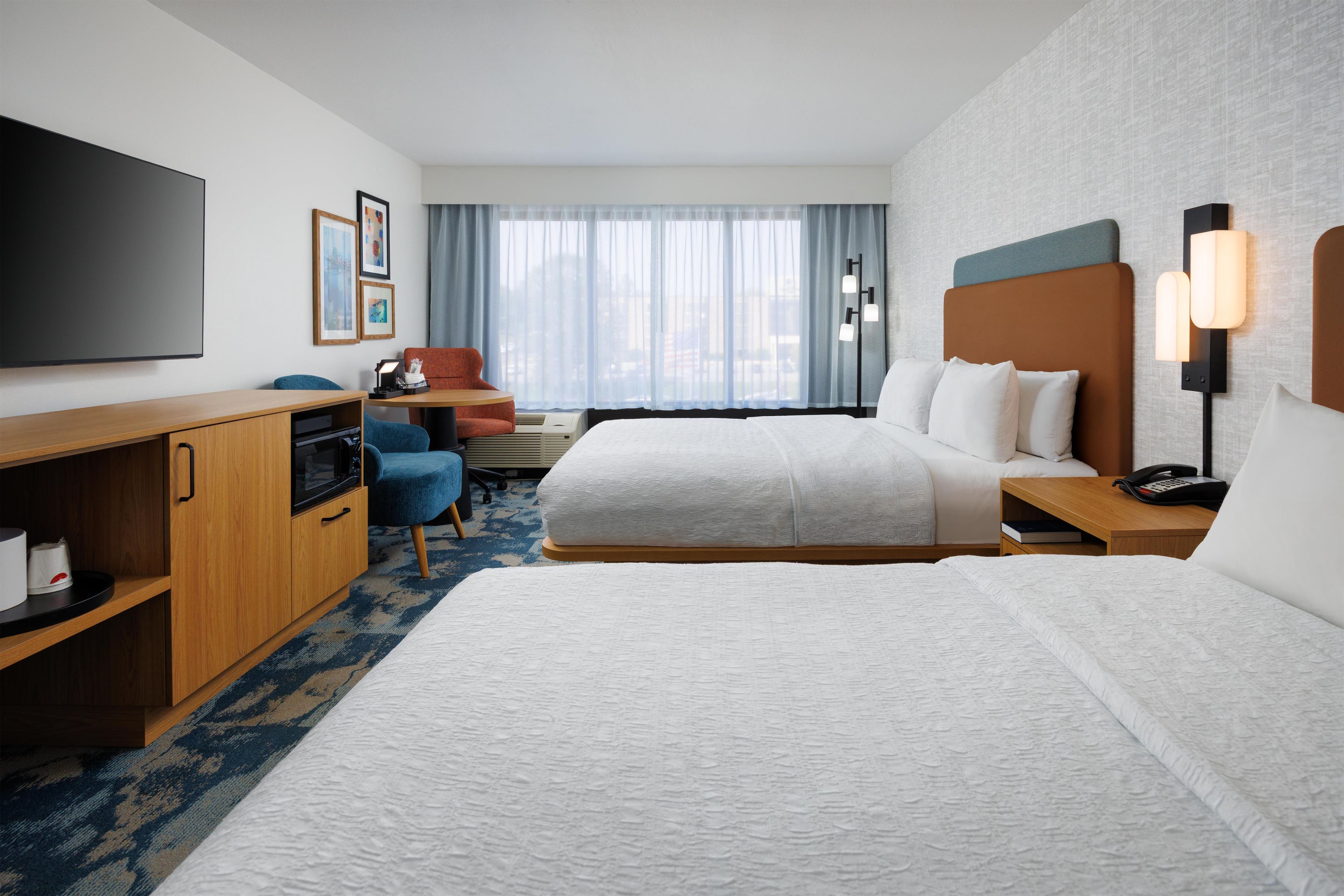 Habitación de hotel con dos camas, un escritorio, un televisor y una ventana con cortinas.