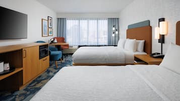 Habitación de hotel con dos camas, un escritorio, un televisor y una ventana con cortinas.