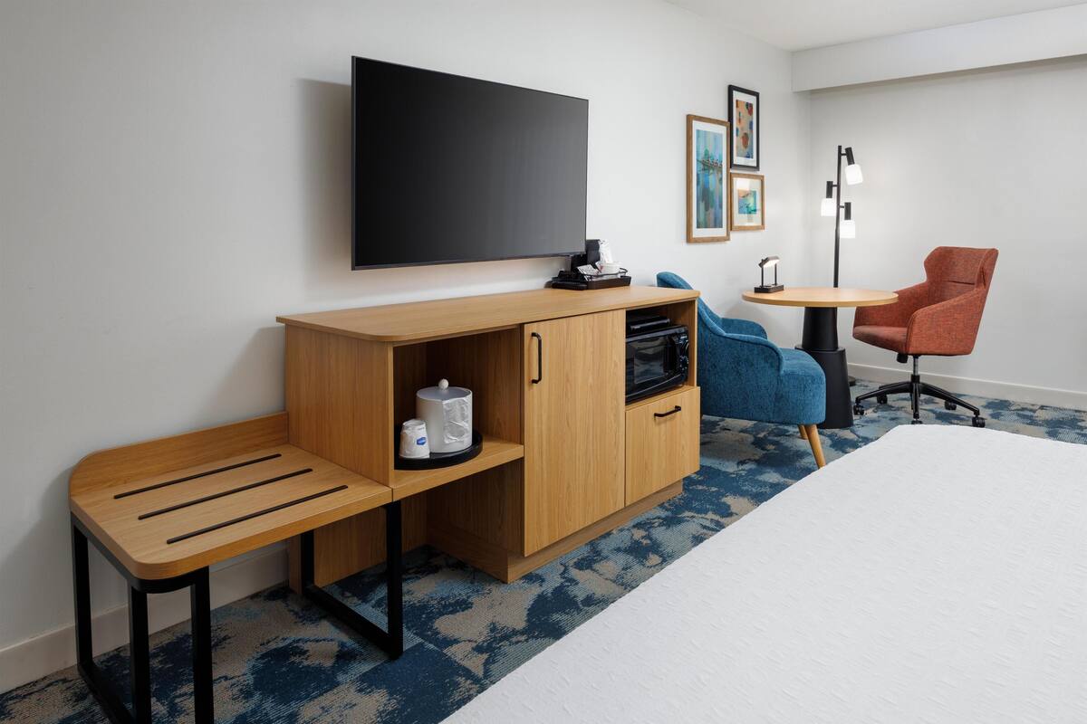 A hotel room with a bed, a desk with a chair, a TV, and a small table with a chair.