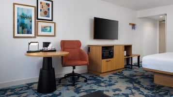 Ein Hotelzimmer mit einem Bett, einem Fernseher, einem Schreibtisch mit Stuhl, einer Mikrowelle und gerahmten Bildern an der Wand.