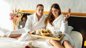 A couple in a hotel room with a tray of breakfast items, a vase of flowers, and a bed with a white headboard. - Domaine de la Forêt d’Orient, Logis Hôtel, Restaurant, Spa & Golf (Rouilly-Sacey)