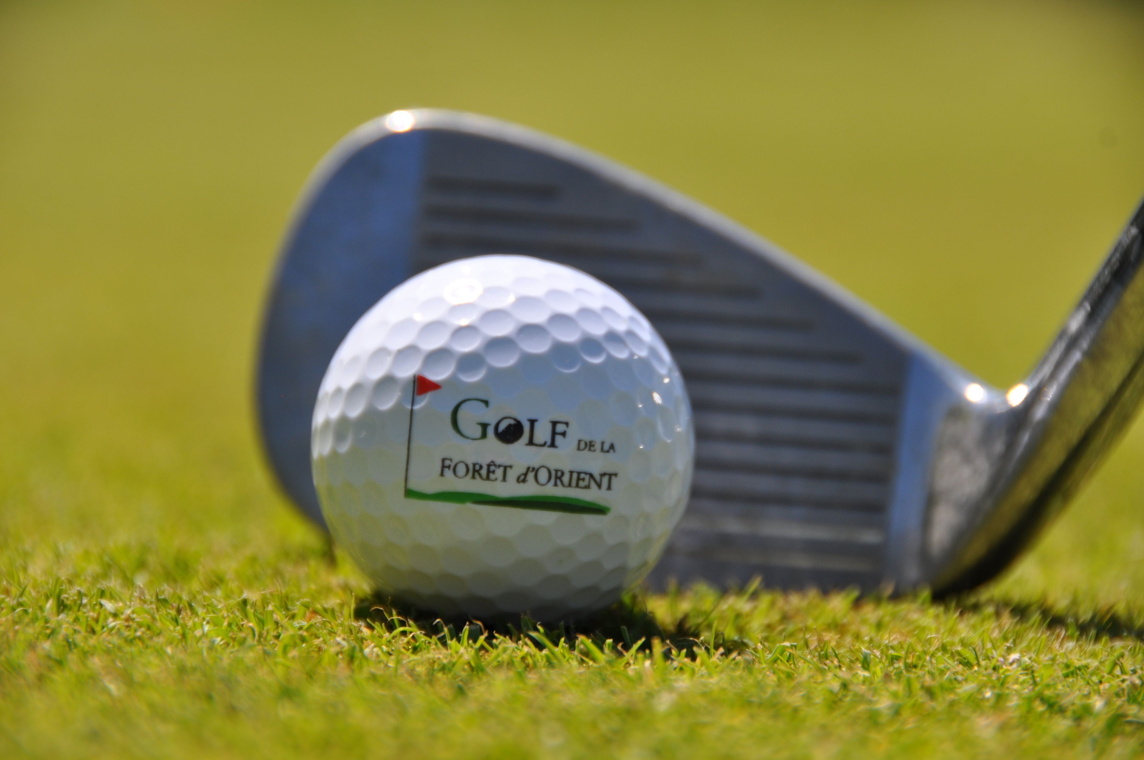 A golf ball with text "GOLF DE LA FORET D'ORIENT" on a grassy surface.