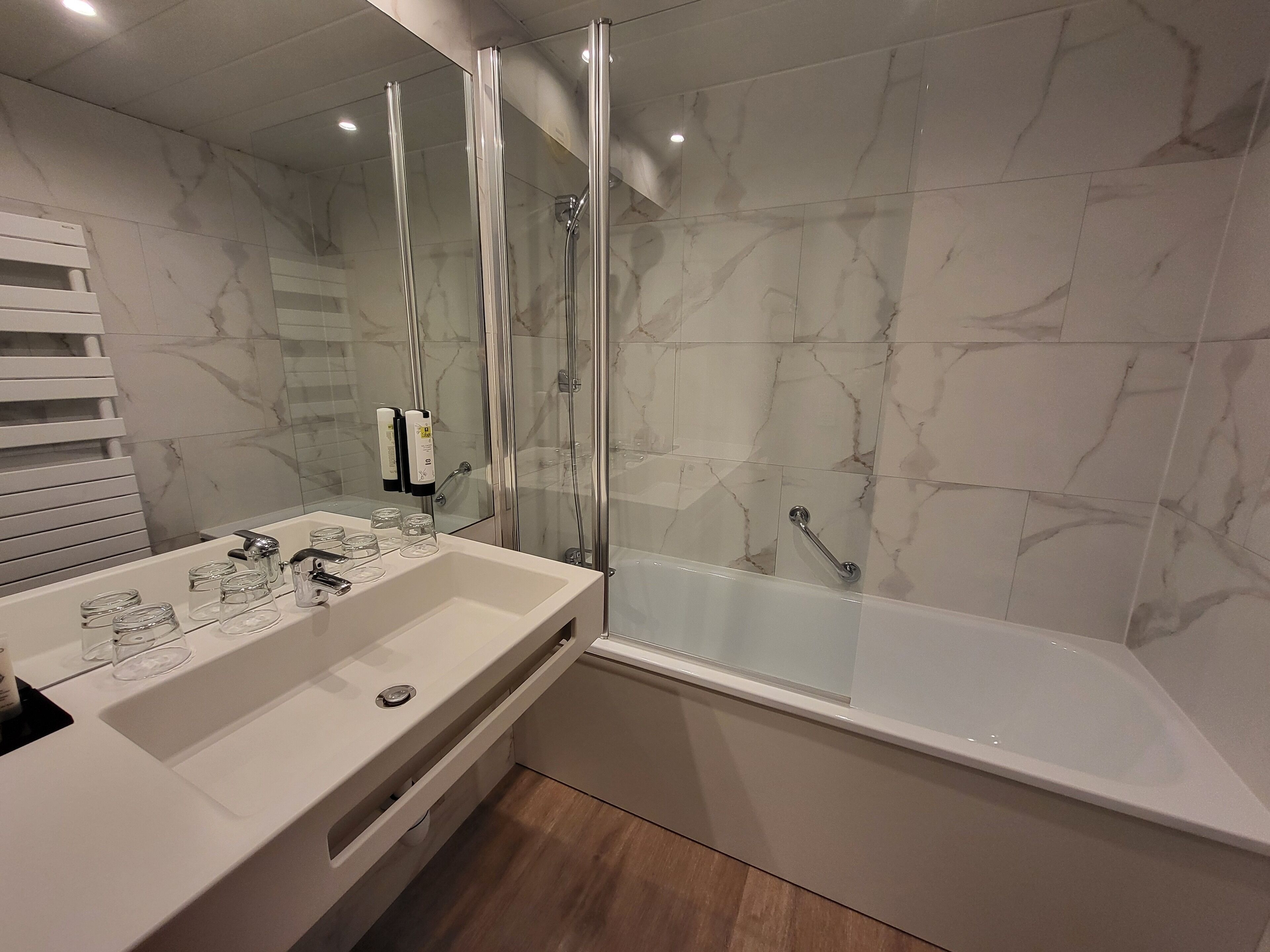 A modern bathroom with a glass-enclosed shower, a white sink with glass containers, and marble-patterned walls.
