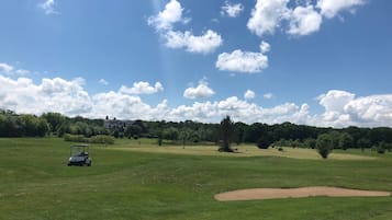 A golf course with a clubhouse, a golf cart, and a clear sky.