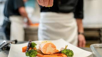 Un chef condimentando un plato con comida, incluyendo brócoli y zanahorias, en una cocina.