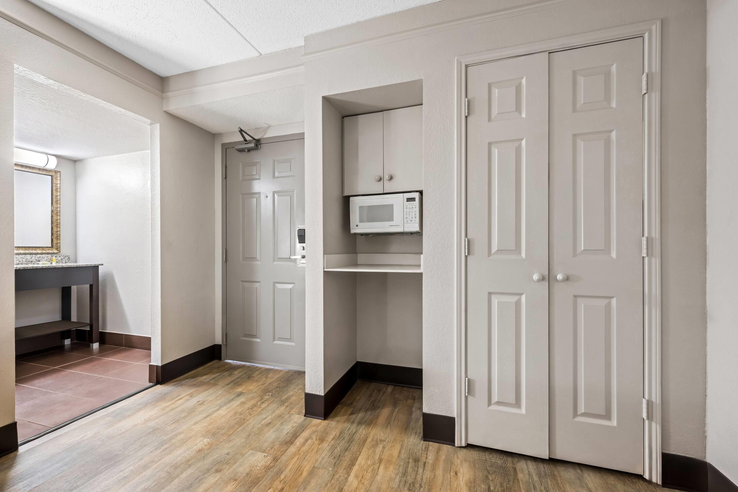 A hallway with a wooden floor, white doors, and a microwave on a shelf.