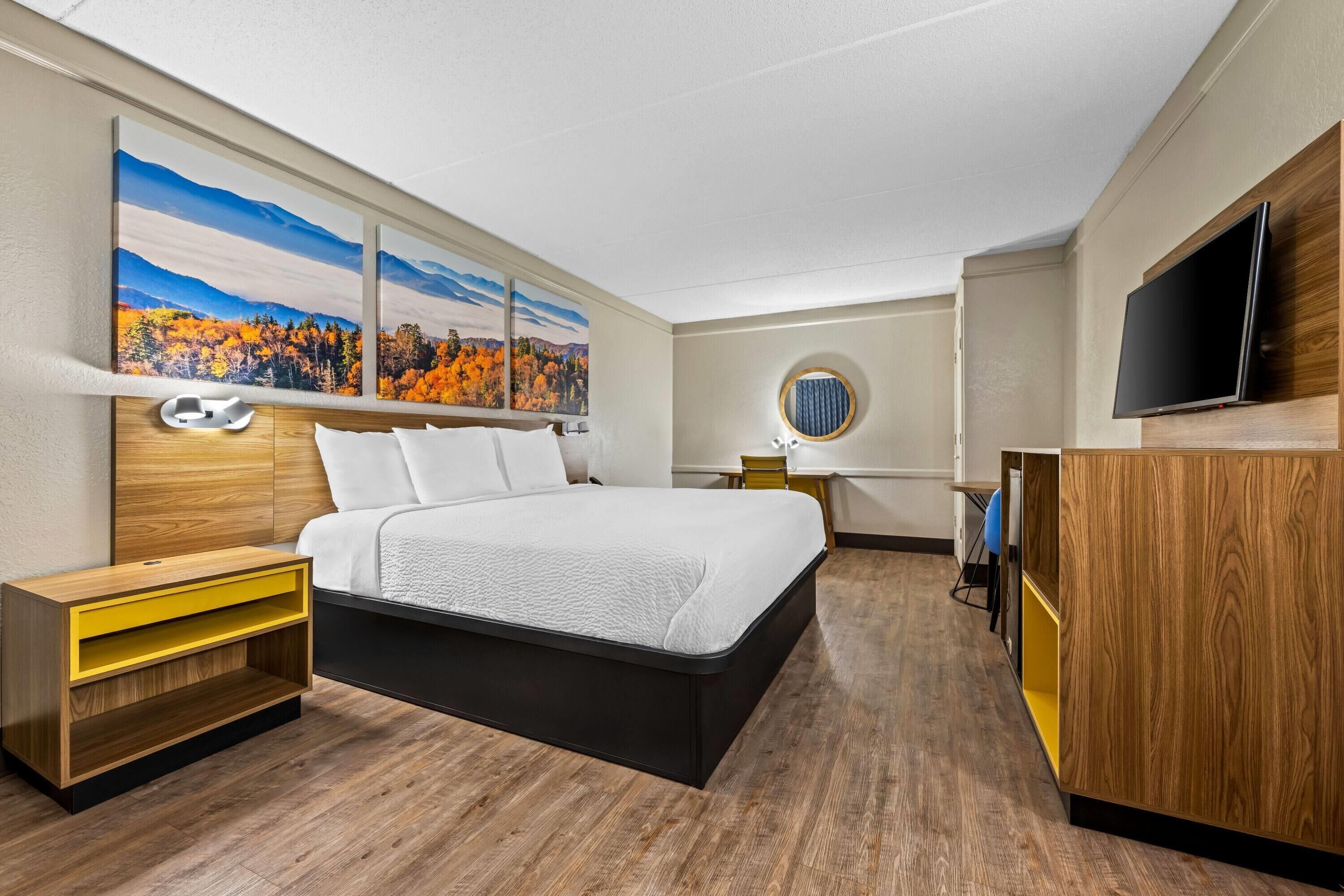 A modern hotel room with a large bed, wooden nightstands, a desk, and a TV.