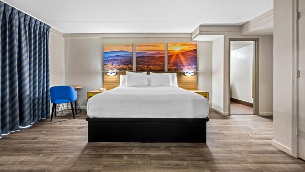 A hotel room with a large bed, a blue chair, a nightstand, and a wall-mounted painting of a sunset. - Days Inn by Wyndham Birmingham/West (Birmingham)
