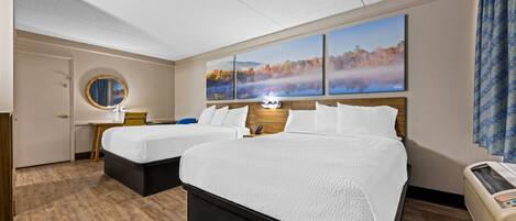 A hotel room with two beds, a round mirror, a nightstand, a wall-mounted TV, and a large window with a view of autumn foliage.
