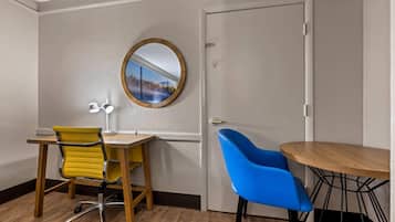 A room with a wooden desk, a yellow office chair, a blue chair, a round mirror, and a door.