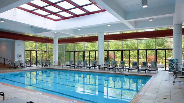 A large indoor swimming pool with multiple lounge chairs and a skylight above. - DoubleTree by Hilton Tulsa - Warren Place (Tulsa)