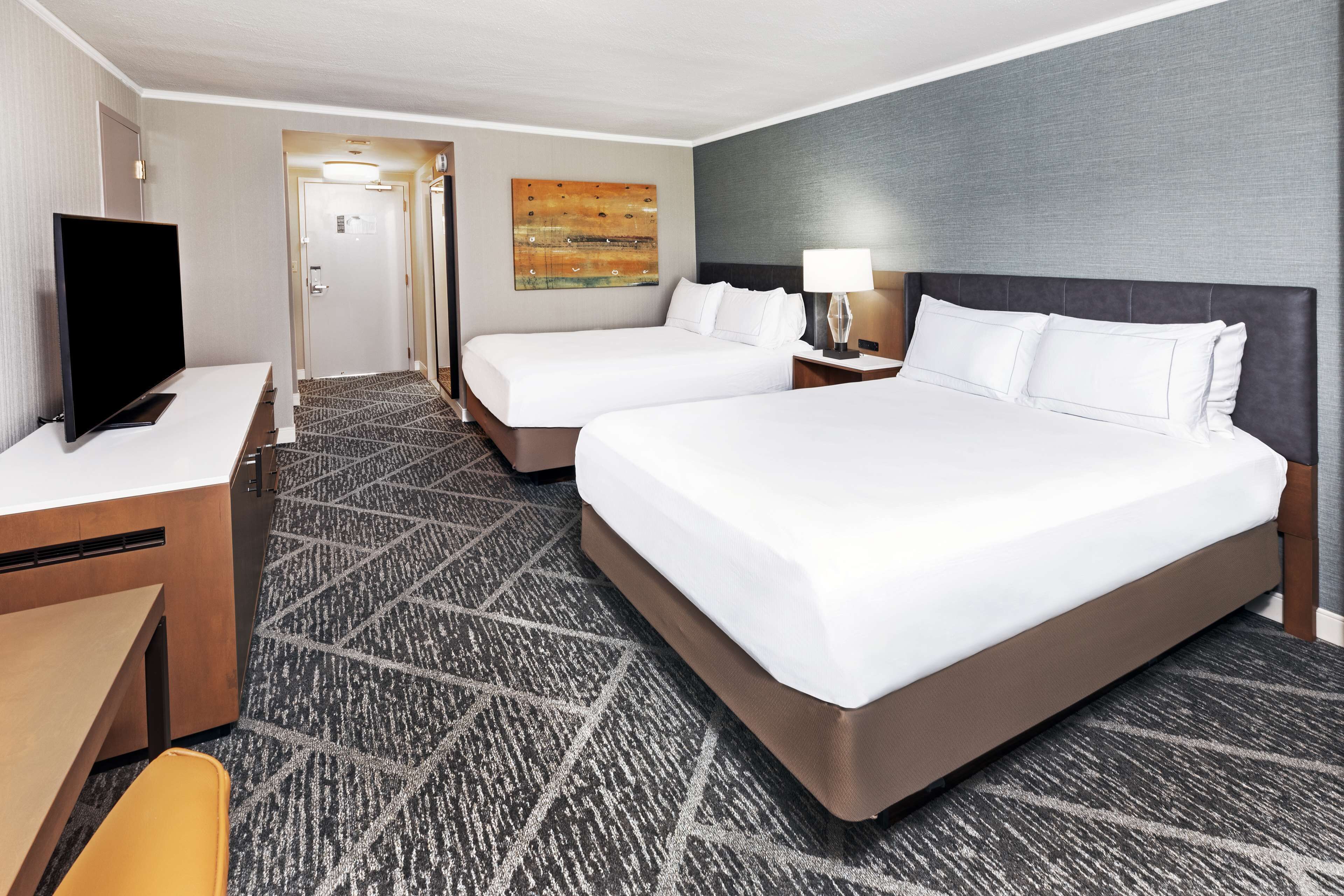 A hotel room with two beds, a desk, a TV, and a carpeted floor.