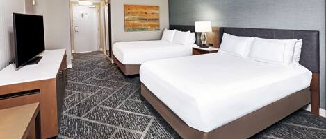 A hotel room with two beds, a desk, a TV, and a carpeted floor.