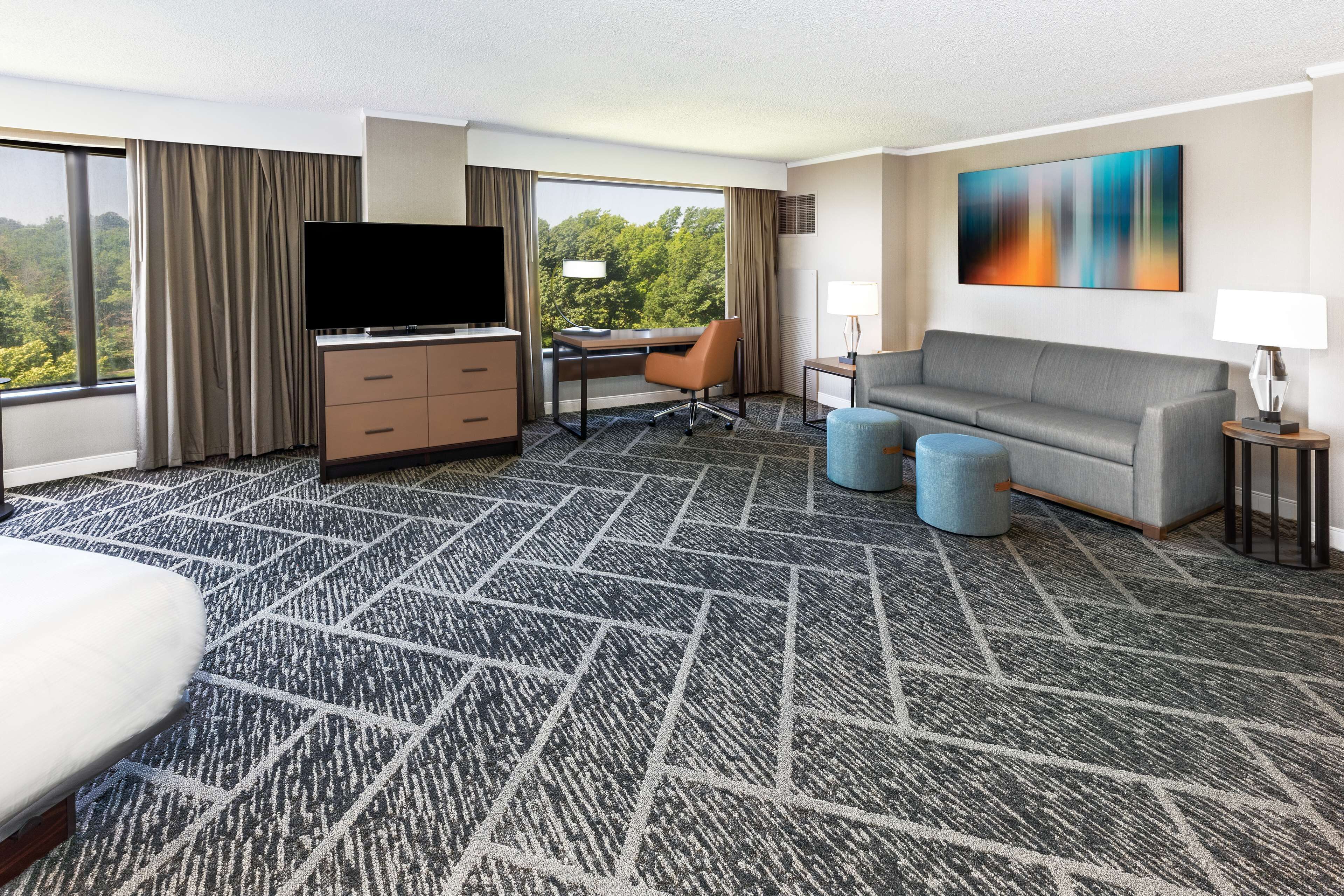 Een hotelkamer met een groot bed, een bureau met stoel, een sofa, een televisie en een schilderij aan de muur.