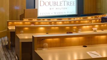A hotel reception area with a large screen displaying the DoubleTree logo and location. There are reception desks with built-in lighting and a carpeted floor.