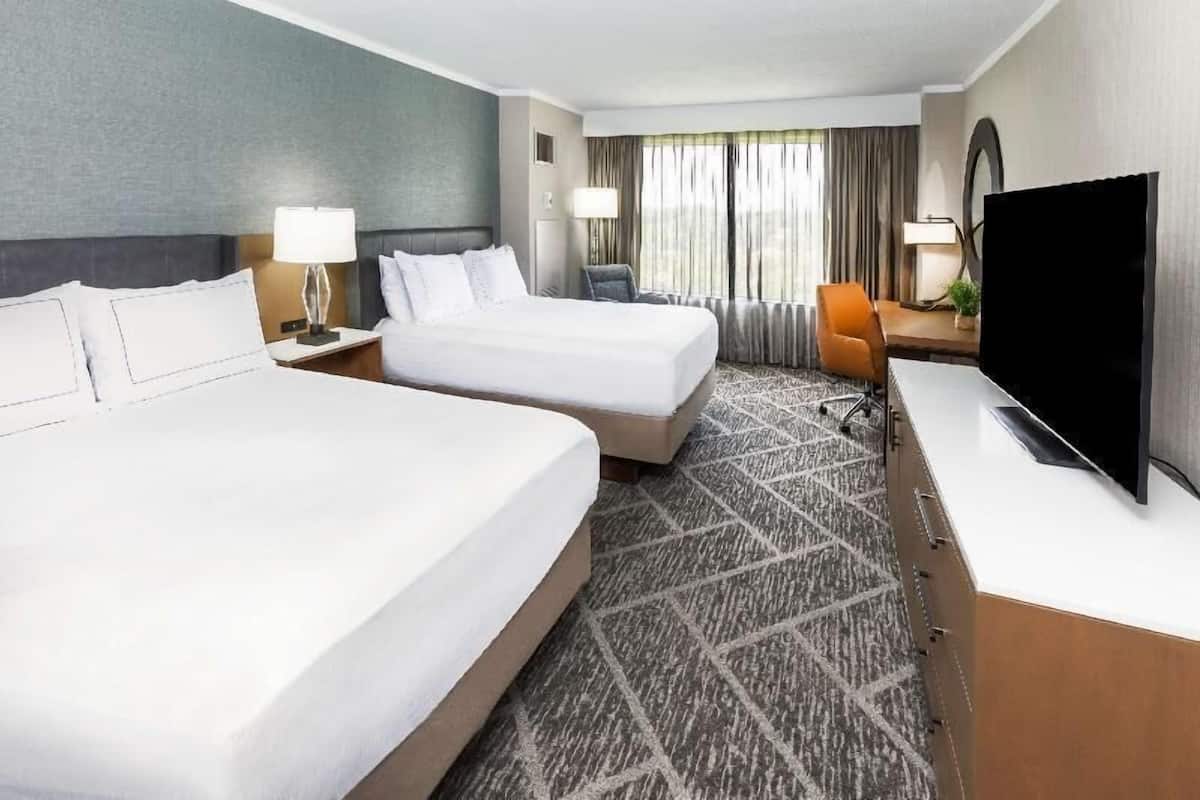 A hotel room with two beds, a desk, a TV, and a window with curtains.