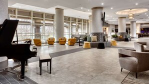 A spacious lobby with a grand piano, modern seating, large windows, and a chandelier. - DoubleTree by Hilton Tulsa - Warren Place (Tulsa)