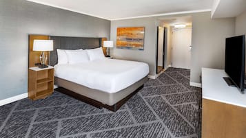 A hotel room with a large bed, a nightstand with a lamp, a television, and a carpeted floor.