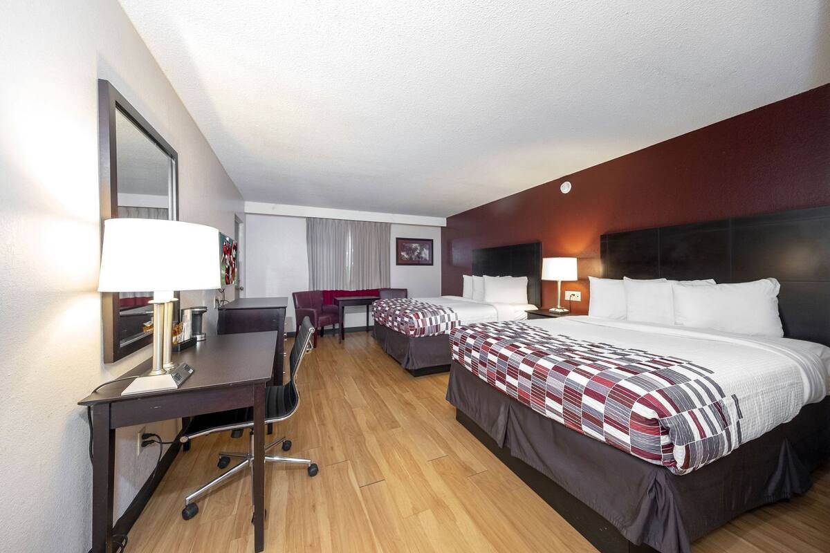 Une chambre d’hôtel avec deux lits, un bureau, une chaise et un grand miroir.