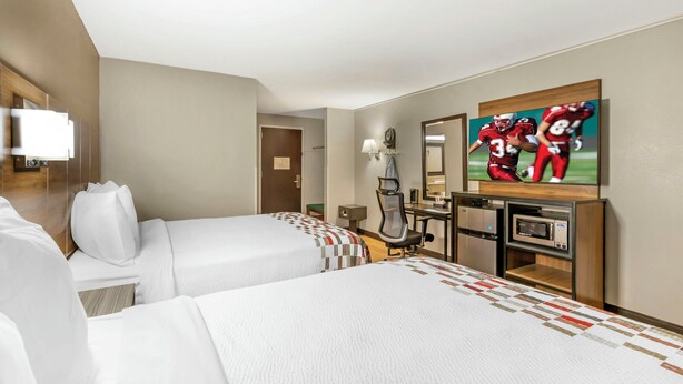 A hotel room with two beds, a desk with a computer, a microwave, and a TV displaying a football game. - Red Roof Inn Lumberton (Lumberton)